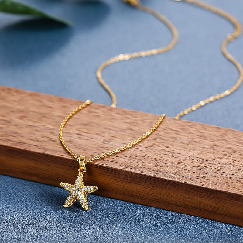 Gold-tone pave starfish pendant necklace resting on a wooden plank over blue textured surface