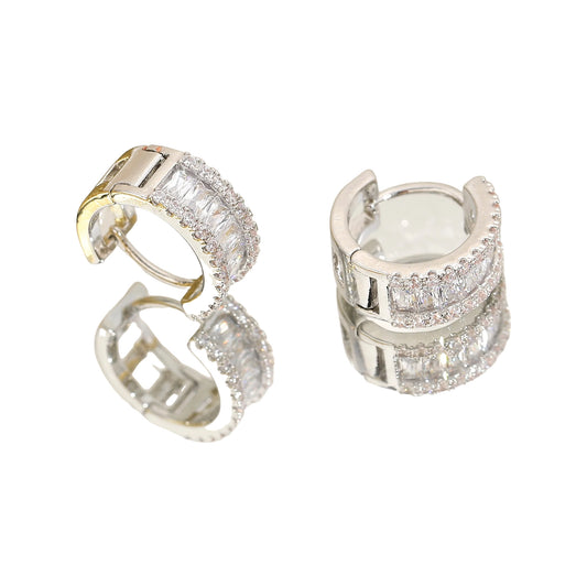 silver-tone baguette rhinestone huggie hoops on a mirrored surface with sheer fabric