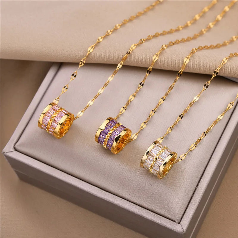 Three barrel pendant necklaces with baguette crystal rows in amber, purple, and clear on a display box, gold-tone chains