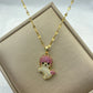 Gold-tone playful doll pendant necklace with pink and clear stones laid on a display box