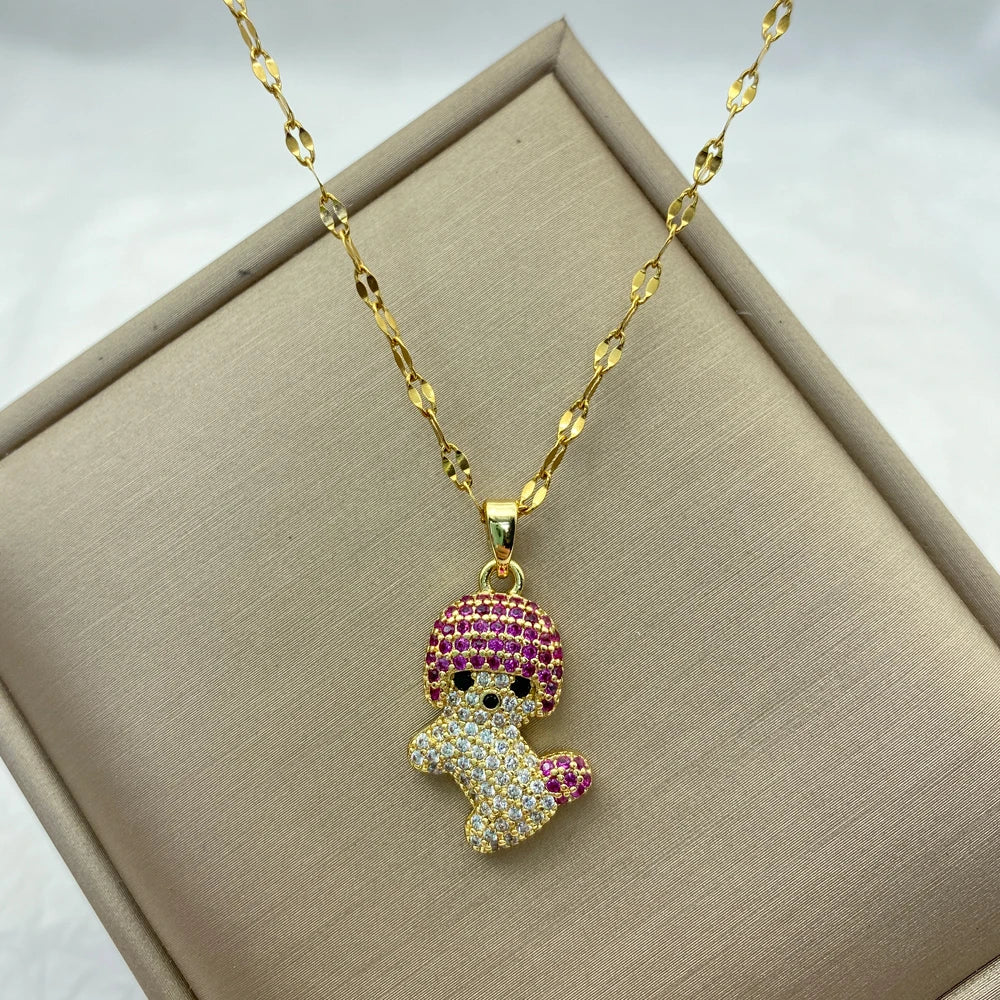 Gold-tone playful doll pendant necklace with pink and clear stones laid on a display box