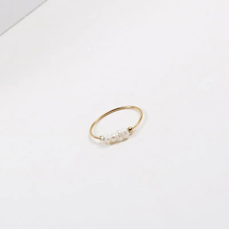 Gold-tone thin stacking ring with irregular pearl beads centered on white surface
