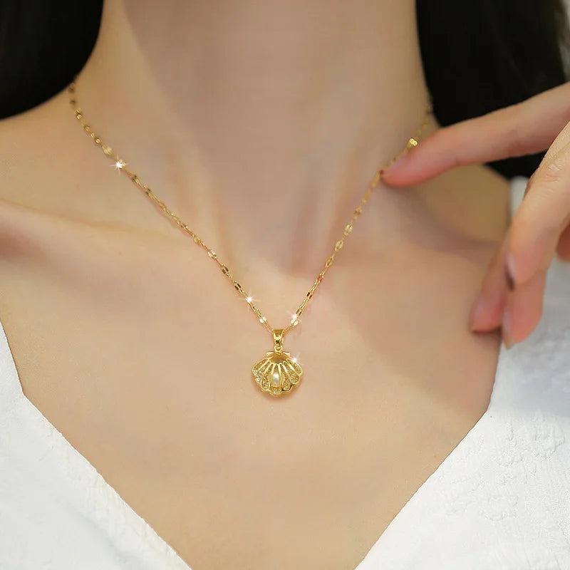 Model wearing a gold-tone scallop shell pendant necklace with pearl-like accent resting at the collarbone.