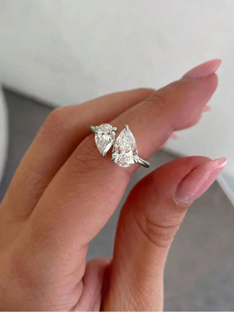 two pear-cut stones set on a gold-tone bypass band displayed between fingertips