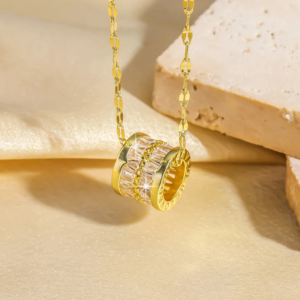 Close-up of a gold-tone barrel pendant necklace with clear baguette crystal rows hanging from a patterned chain