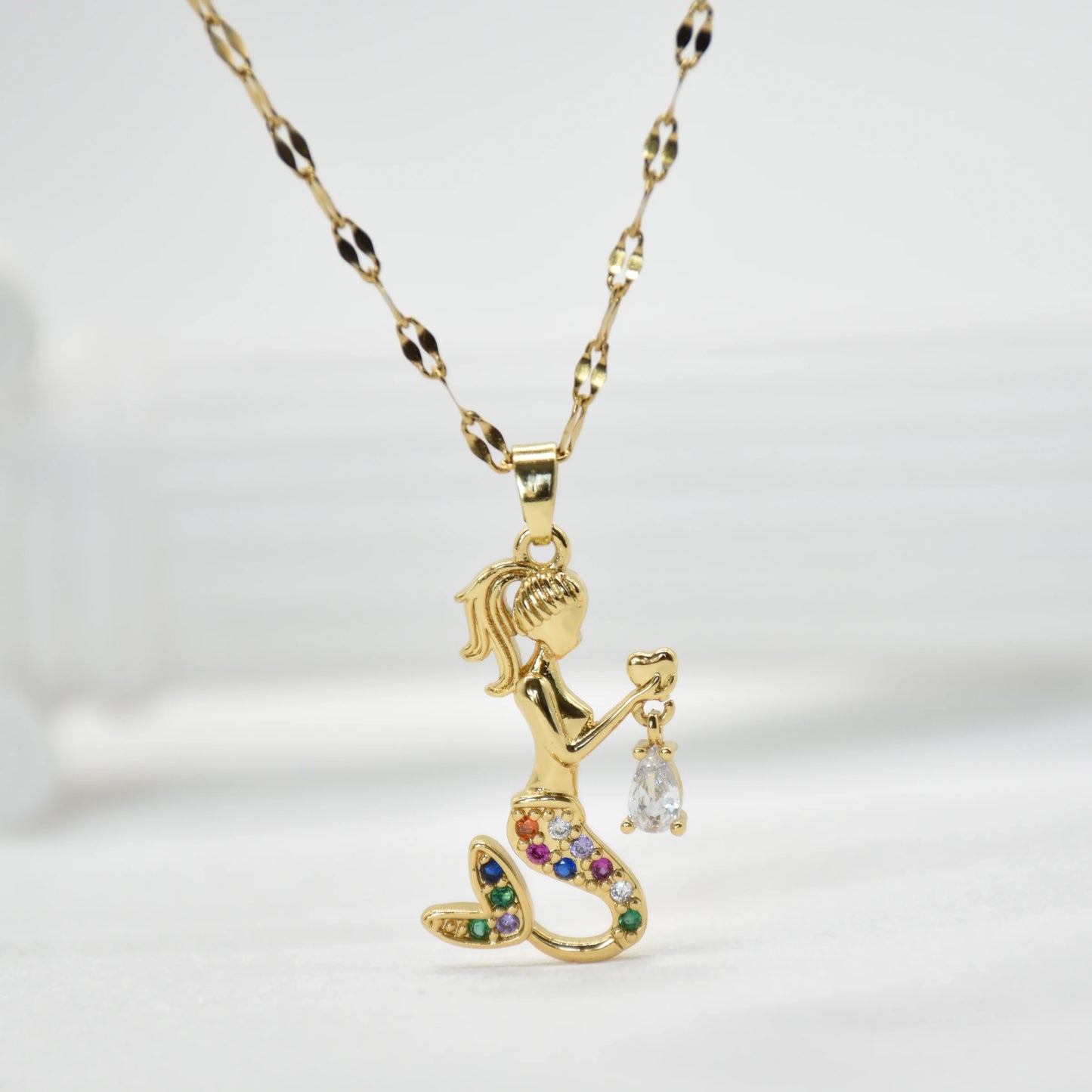 Gold-tone mermaid pendant necklace with multicolored stone accents holding a small dangling stone