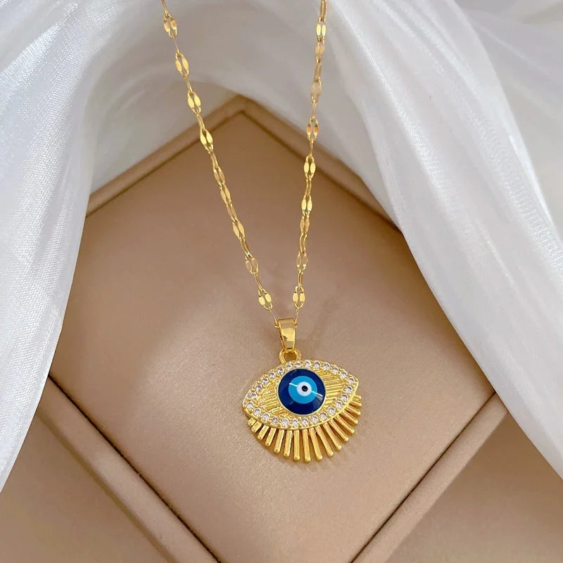 Gold-tone eye pendant with blue center and radiant fringe resting on a beige cushion