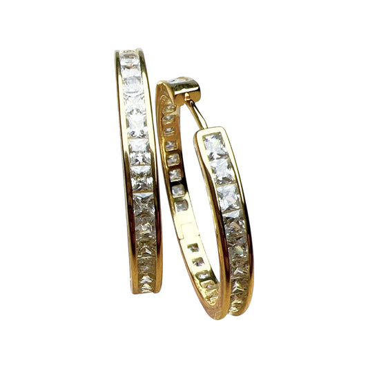 Gold-tone hinged hoop earrings with clear stones displayed on a textured pastel background
